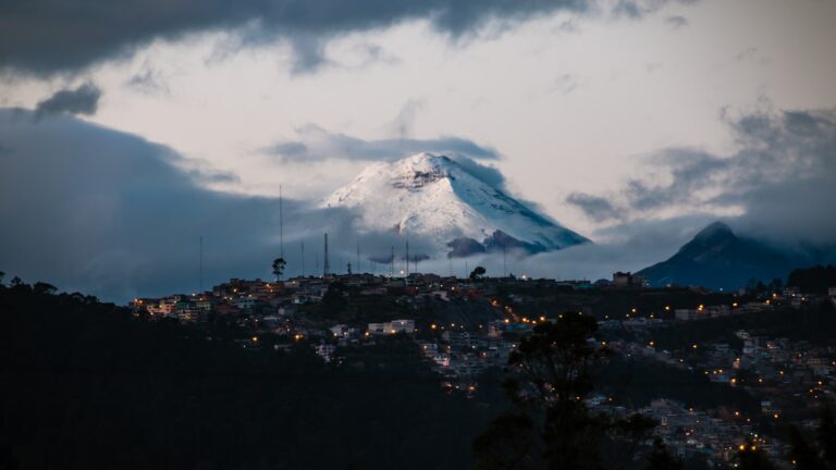 Cotopaxi volcano at dawn towering over the lit-up hillside neighborhoods of Quito, Ecuador
